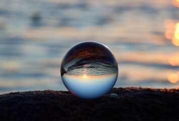 Crystal ball on rocky beach on a granite boulder, sunset reflecting in the sea, background blurred