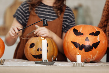 Happy Halloween. little child girl are preparing to Halloween on kitchen. pumpkin Jack lanterns with carved smile and candle for family holiday at home. Kid is having fun with pumpkins.