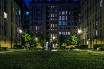 Night park paths and colored houses at summer night. Night paths, benches and lanterns in a...