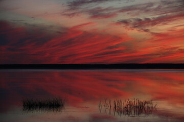 Red sunset over the river, fiery stains in the painted sky, mirrored on the calm surface of the...