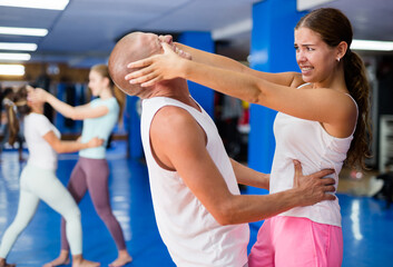 Concentrated young female practicing effective self defence techniques with coach in training room