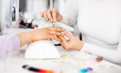 Young woman hands in a nail salon, which the manicure master files the nails with a nail file, giving them shape - Powered by Adobe