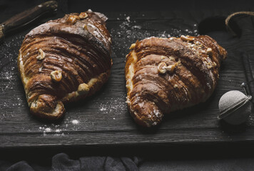 Baked croissant on a  board and sprinkled with powdered sugar, black table. Appetizing pastries for breakfast.