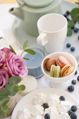 Fototapeta na wymiar Macarons in white bowl, candles, meringue, teapot and pink roses on the table, tea party with sweets