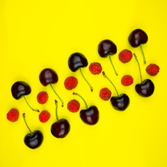 Diagonal  lines of  dark red cherries with green stems and red and pink raspberries on a yellow field.