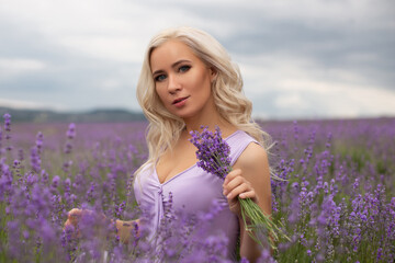 Fototapeta na wymiar Young beautiful blonde woman with long wavy hair in violet dress in lavender field, natural beauty 