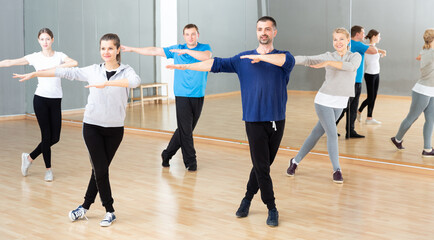 Fototapeta na wymiar Group of different ages women and men doing stretching exercises warming up at dance class