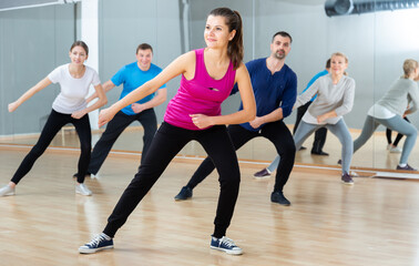 Fototapeta na wymiar Portrait of young emotional woman doing exercises during group class in dance center