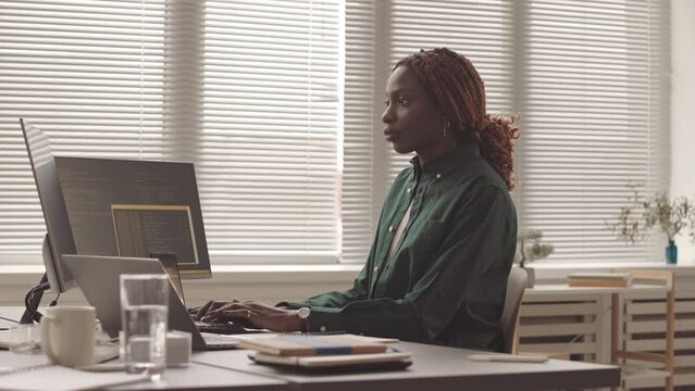 Medium slowmo of young African American female programmer smiling at camera while writing program code on computer at workplace
