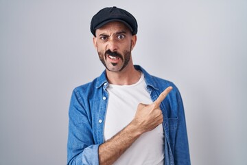 Hispanic man with beard standing over isolated background pointing aside worried and nervous with forefinger, concerned and surprised expression