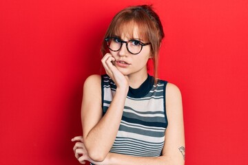 Redhead young woman wearing casual clothes and glasses looking stressed and nervous with hands on mouth biting nails. anxiety problem.