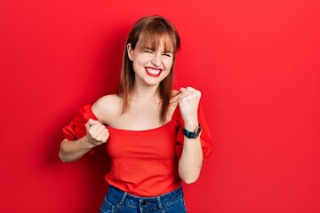Redhead young woman wearing casual red t shirt celebrating surprised and amazed for success with arms raised and eyes closed. winner concept.