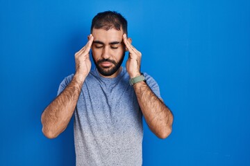 Naklejka premium Middle east man with beard standing over blue background with hand on head, headache because stress. suffering migraine.