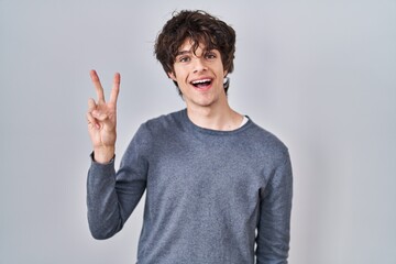 Fototapeta premium Young man standing over isolated background showing and pointing up with fingers number two while smiling confident and happy.