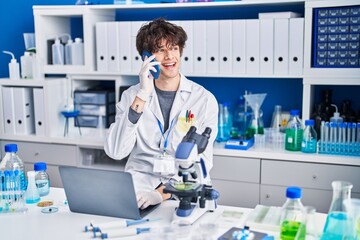 Young hispanic man scientist talking on the smartphone using laptop at laboratory