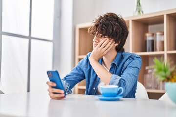 Young hispanic man using smartphone with serious expression at home