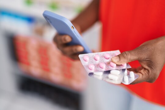 African american woman customer using smartphone holding pills at pharmacy