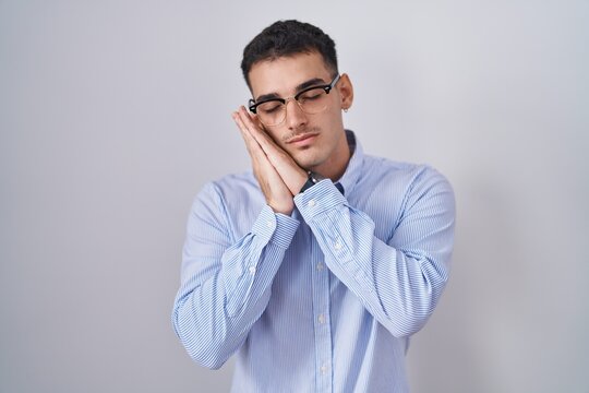 Handsome hispanic man wearing business clothes and glasses sleeping tired dreaming and posing with hands together while smiling with closed eyes.