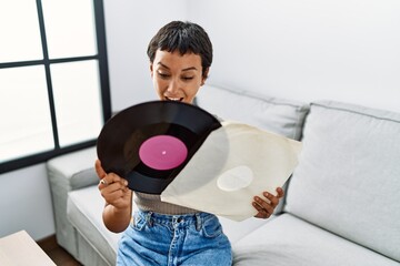 Young hispanic woman smiling confident holding vinyl disc at home