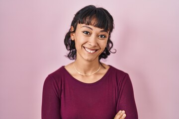 Young beautiful woman standing over pink background happy face smiling with crossed arms looking at the camera. positive person.