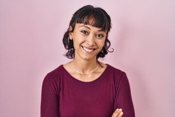 Fototapeta premium Young beautiful woman standing over pink background happy face smiling with crossed arms looking at the camera. positive person.