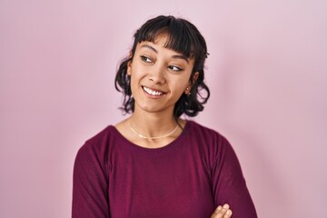 Young beautiful woman standing over pink background looking away to side with smile on face, natural expression. laughing confident.