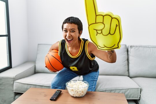 Young hispanic woman smiling confident supporting basketbal game at home