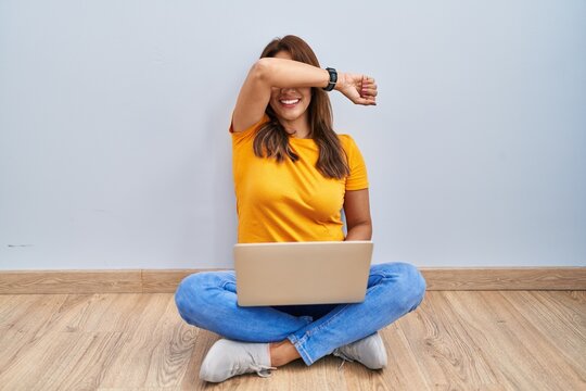 Hispanic Woman Using Laptop Sitting On The Floor At Home Smiling Cheerful Playing Peek A Boo With Hands Showing Face. Surprised And Exited