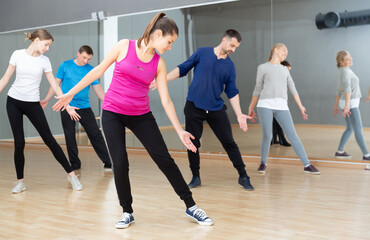 Fototapeta na wymiar Smiling females and males doing Zumba dance workout during group classes in fitness center
