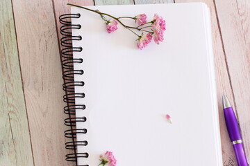 Blank notebook page with flowers and pen on wooden table