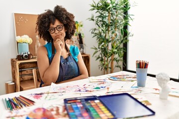 Beautiful african american woman with afro hair painting at art studio looking confident at the camera with smile with crossed arms and hand raised on chin. thinking positive.