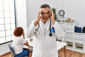 Middle age doctor man at the clinic with a patient with hand on head for pain in head because stress. suffering migraine.