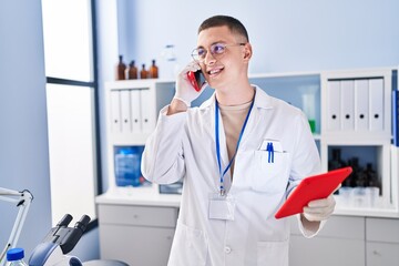 Young hispanic man scientist talking on smartphone using touchpad at laboratory