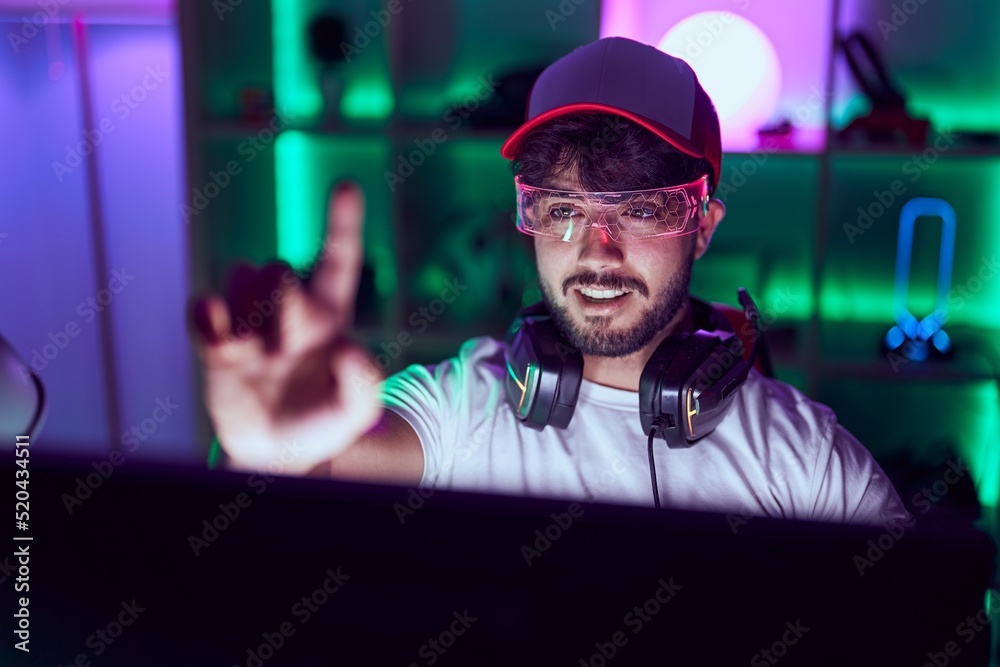 Sticker Young hispanic man streamer smiling confident using virtual reality glasses at gamin room