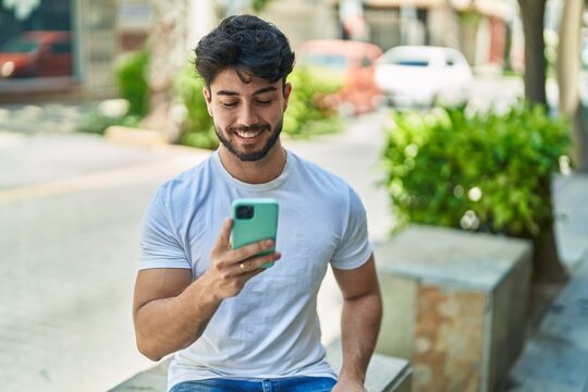 Young hispanic man smiling confident using smartphone at street
