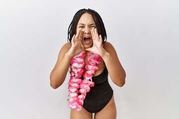 Young african american woman wearing swimsuit and hawaiian lei shouting angry out loud with hands...