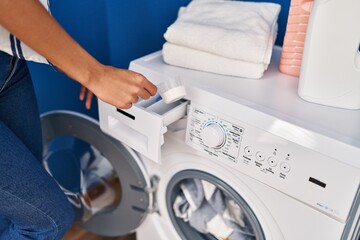 Young blonde woman pouring detergent on washing machine at laundry room