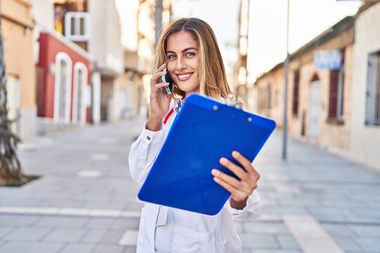 Young blonde woman wearing doctor uniform talking on the smartphone at street