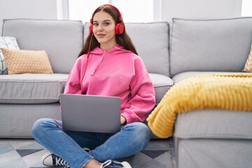 Young woman using smartphone and headphones sitting on floor at home