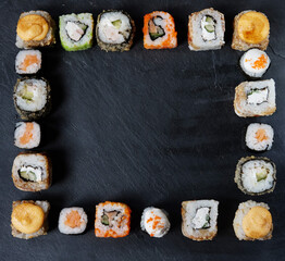 A variety of sushi with wooden desk on black slate background. Asian food frame.