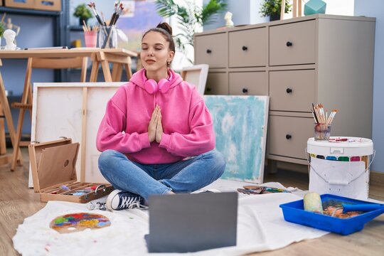 Young woman artist sitting on floor doing yoga exercise at art studio