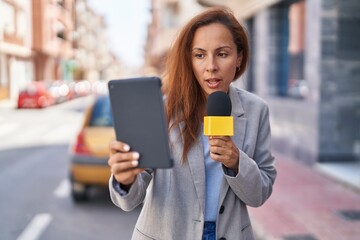 Young woman reporter working using microphone and touchpad at street