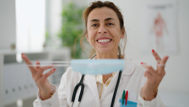 Middle age hispanic woman wearing doctor uniform holding medical mask at clinic