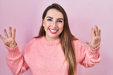 Young hispanic woman standing over pink background showing and pointing up with fingers number nine...