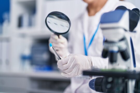 Young beautiful hispanic woman scientist looking test tube with loupe at laboratory