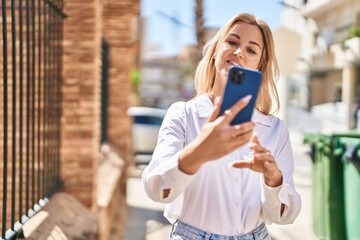 Young blonde woman smiling confident using smartphone at street