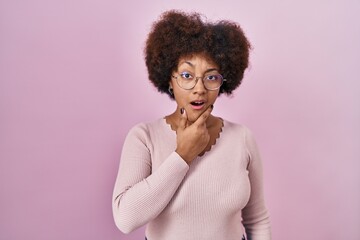 Young african american woman standing over pink background looking fascinated with disbelief, surprise and amazed expression with hands on chin