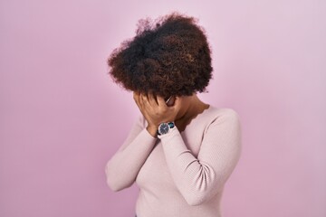 Young african american woman standing over pink background with sad expression covering face with hands while crying. depression concept.