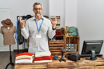 Middle age hispanic man working as manager at retail boutique shouting with crazy expression doing rock symbol with hands up. music star. heavy music concept.