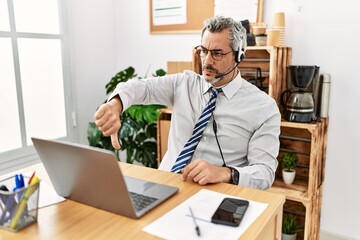 Fototapeta premium Middle age hispanic business man working at the office wearing operator headset looking unhappy and angry showing rejection and negative with thumbs down gesture. bad expression.